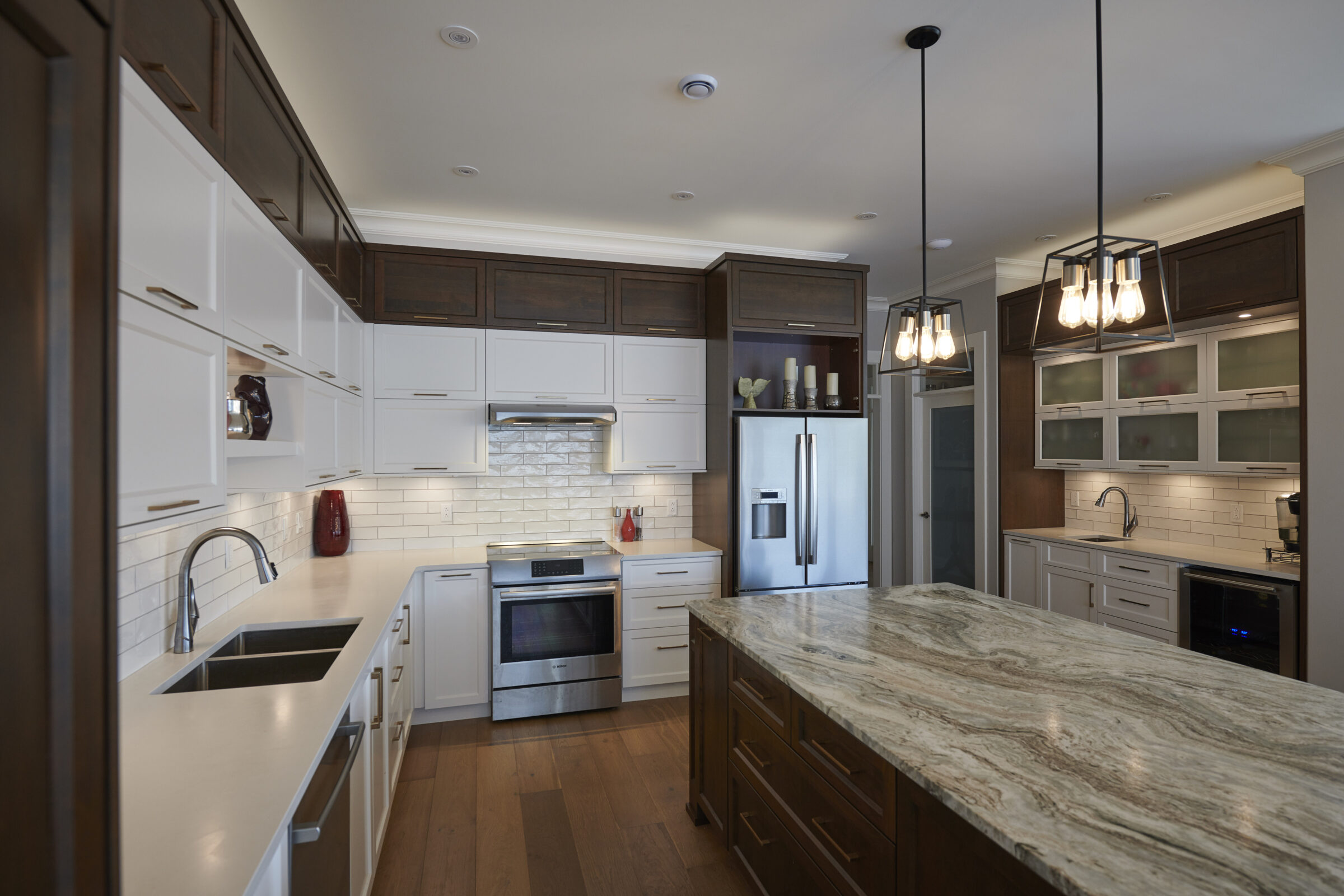 Modern kitchen with dark wood and white cabinets, stainless steel appliances, granite countertops, and pendant lighting. No people are visible in the space.
