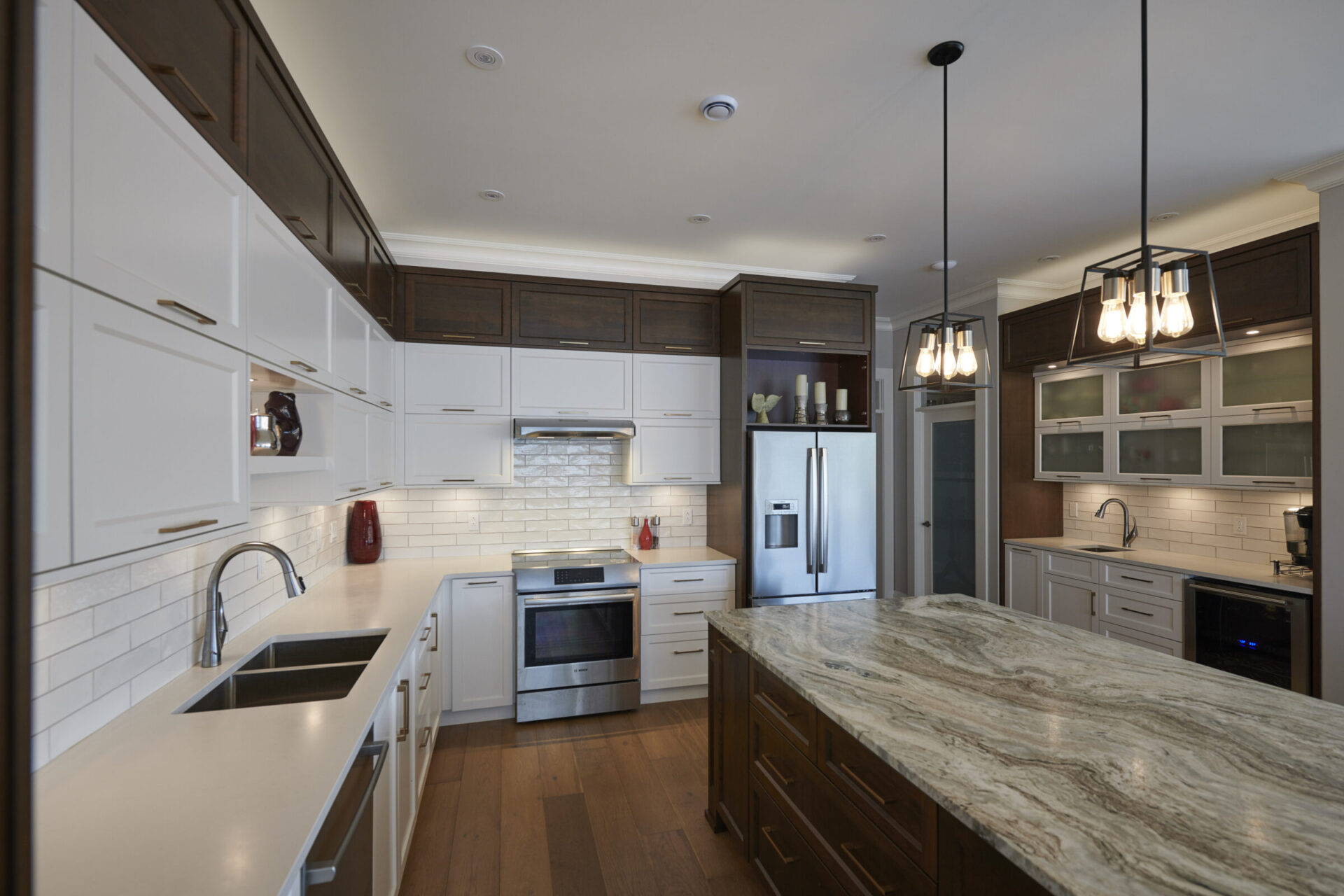 Modern kitchen interior with white cabinetry, dark countertops, stainless steel appliances, hardwood floors, and pendant lighting over an island.