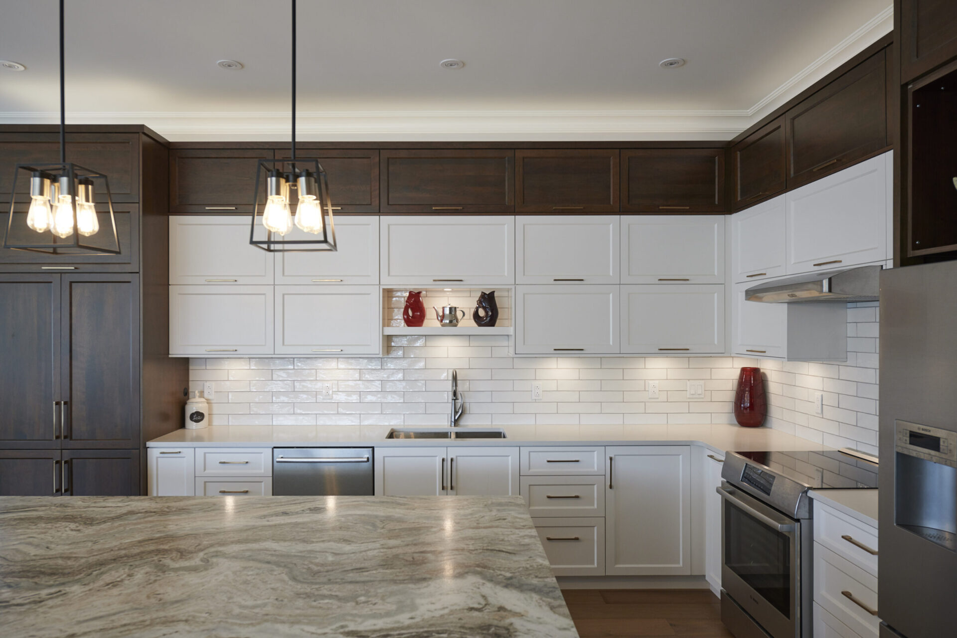 Modern kitchen with white cabinets, dark countertops, stainless steel appliances, subway tiles backsplash, and pendant lights. Clean, stylish interior design.