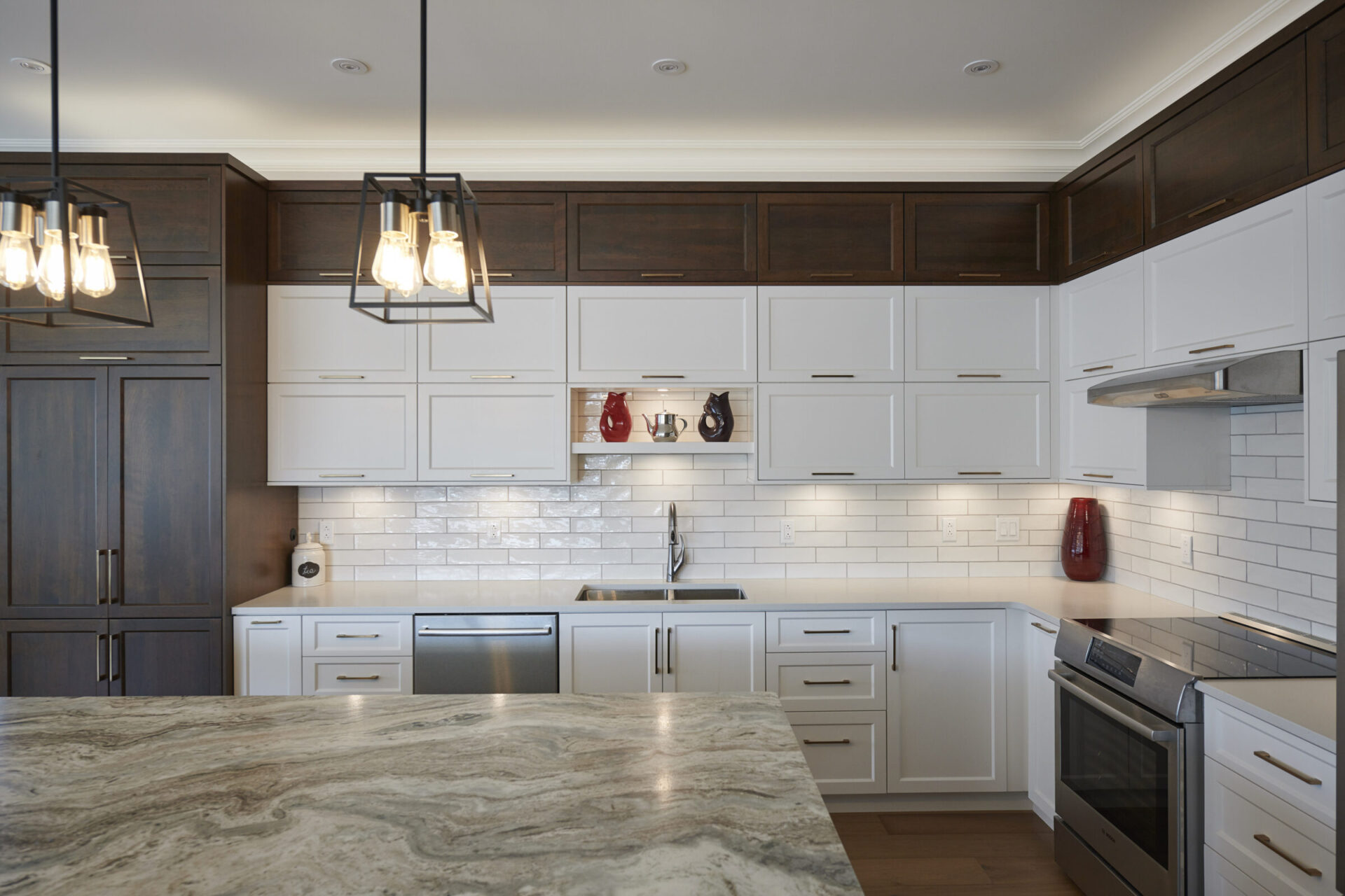 A modern kitchen with white cabinets, stainless steel appliances, dark wood accents, pendant lights, and a marbled countertop island in the foreground.