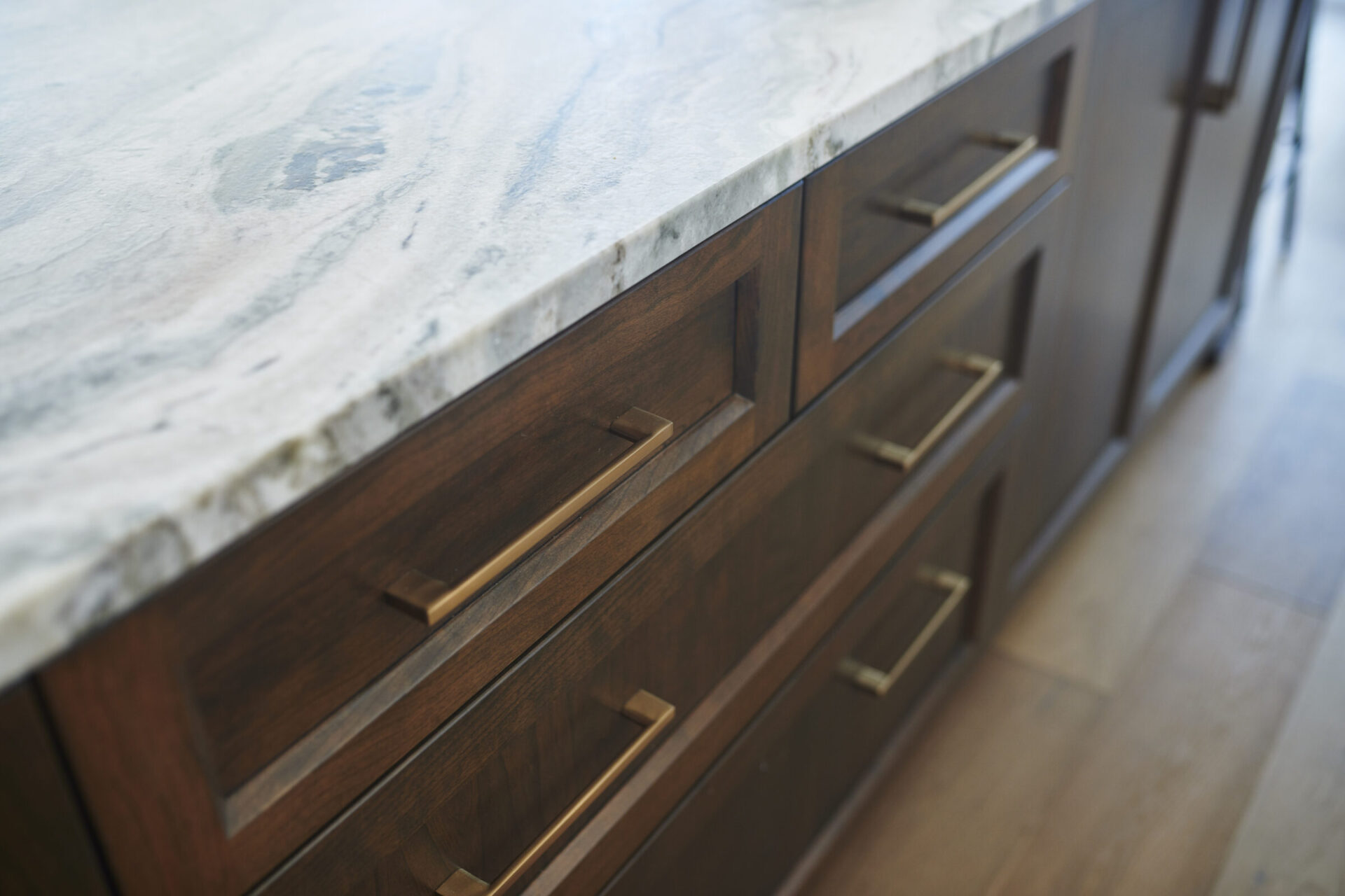 Close-up of a kitchen counter with a marble top and wooden cabinets featuring brass handles, in a modern interior with a shallow depth of field.