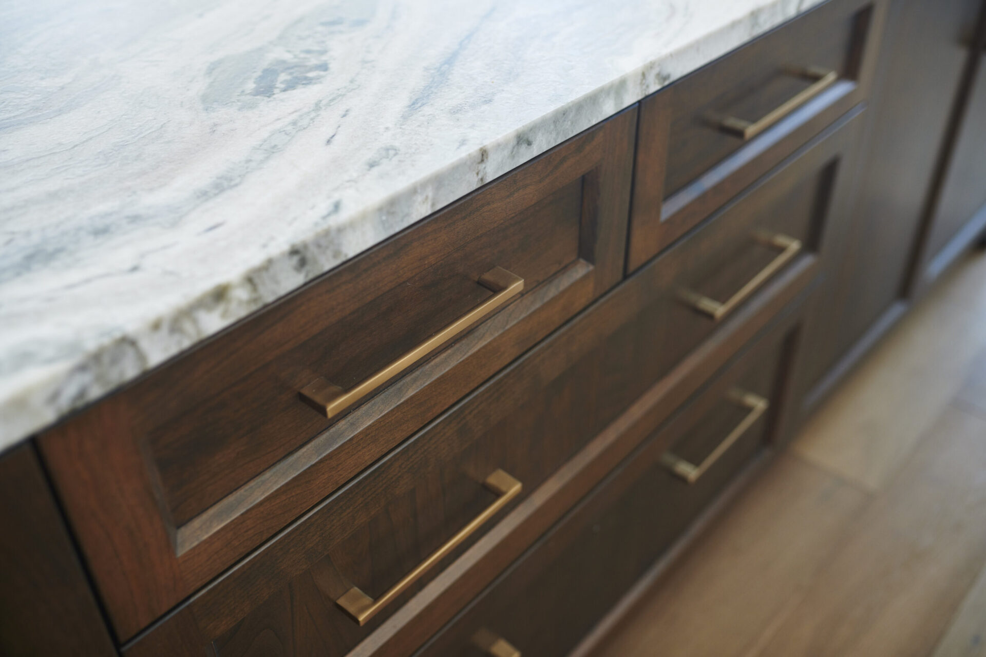 This image shows a close-up of a modern kitchen with wooden cabinets and metal handles, topped by a white marble countertop with grey veining.