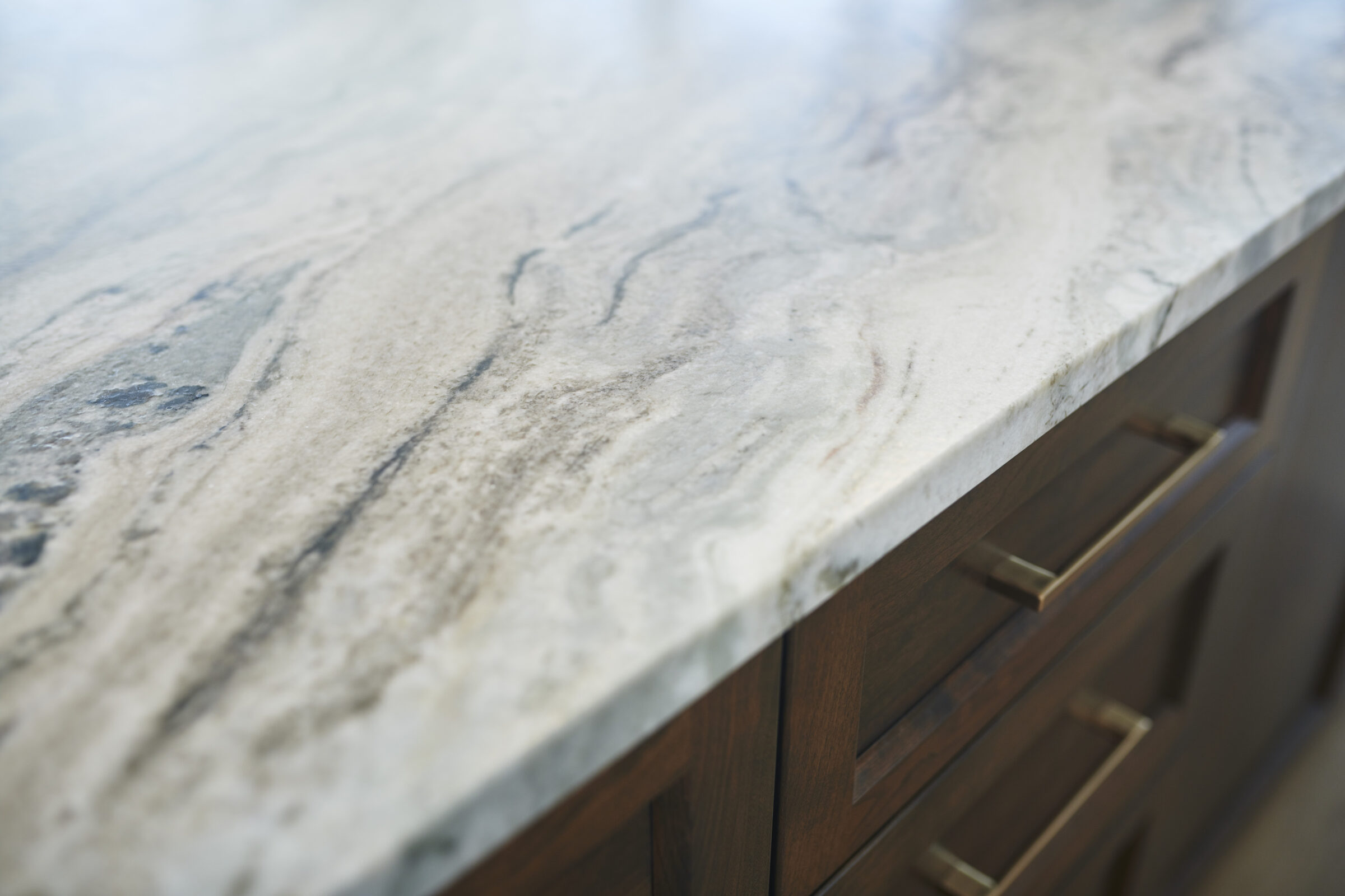 An image showing a close-up of a marble countertop with swirled patterns above wooden drawers with metallic handles. Focus is shallow with blurred background.