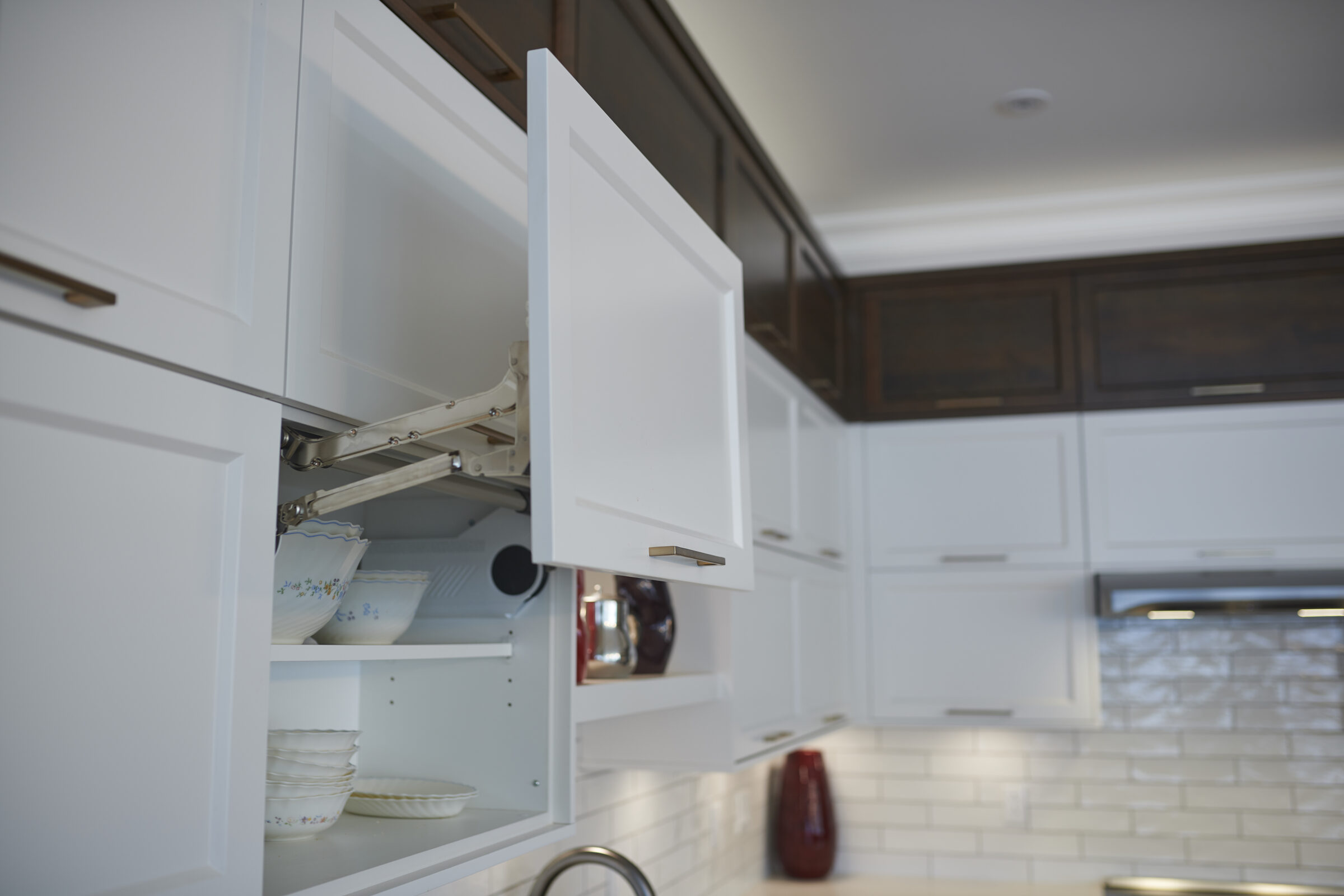 Modern kitchen with white cabinetry, an open upper cabinet with dishes inside, and a subway tile backsplash. Metal handles and hinges are visible.