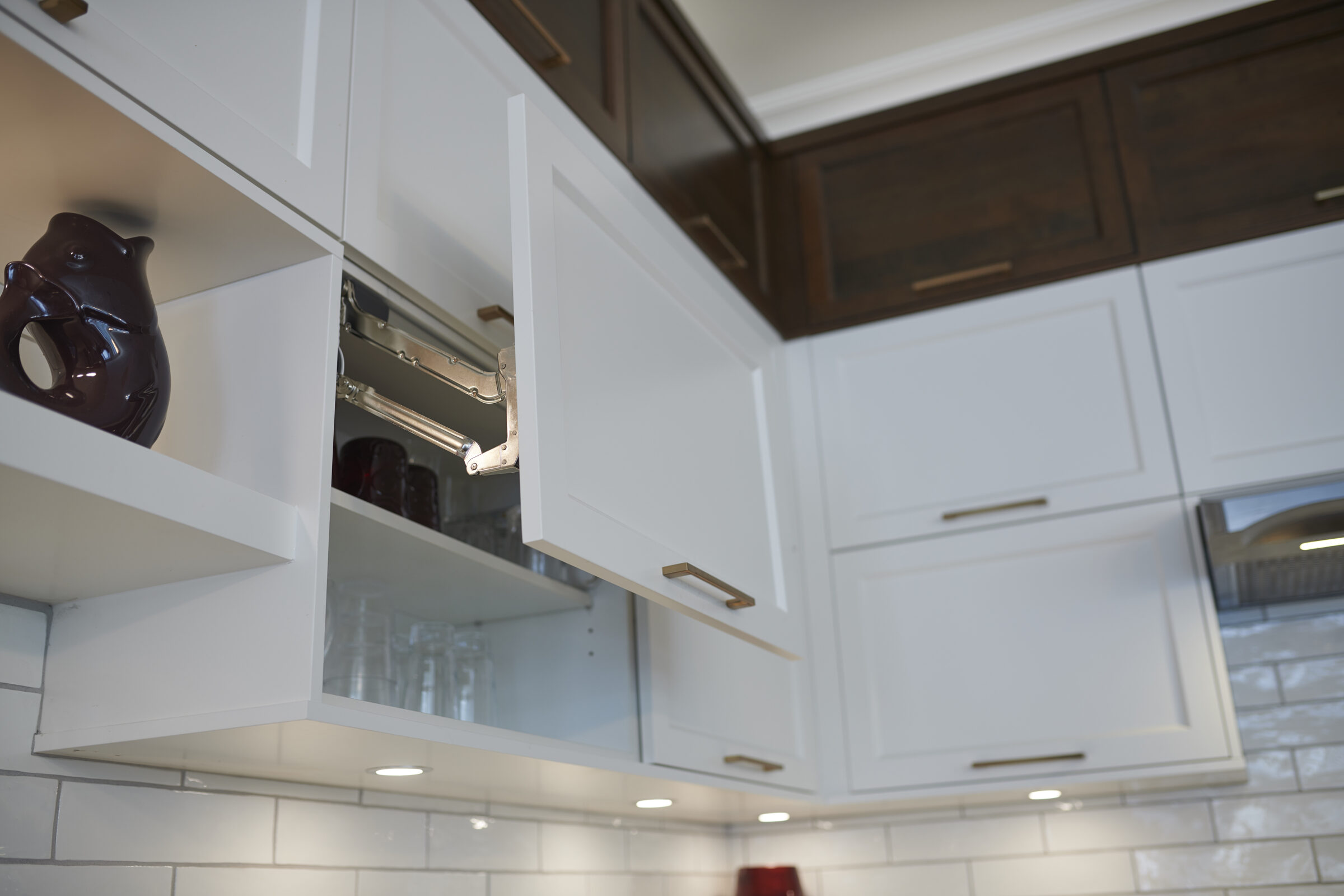 A modern kitchen with white cabinetry and subway tile backsplash, featuring open cabinet doors and a glimpse of stored dinnerware and glasses.