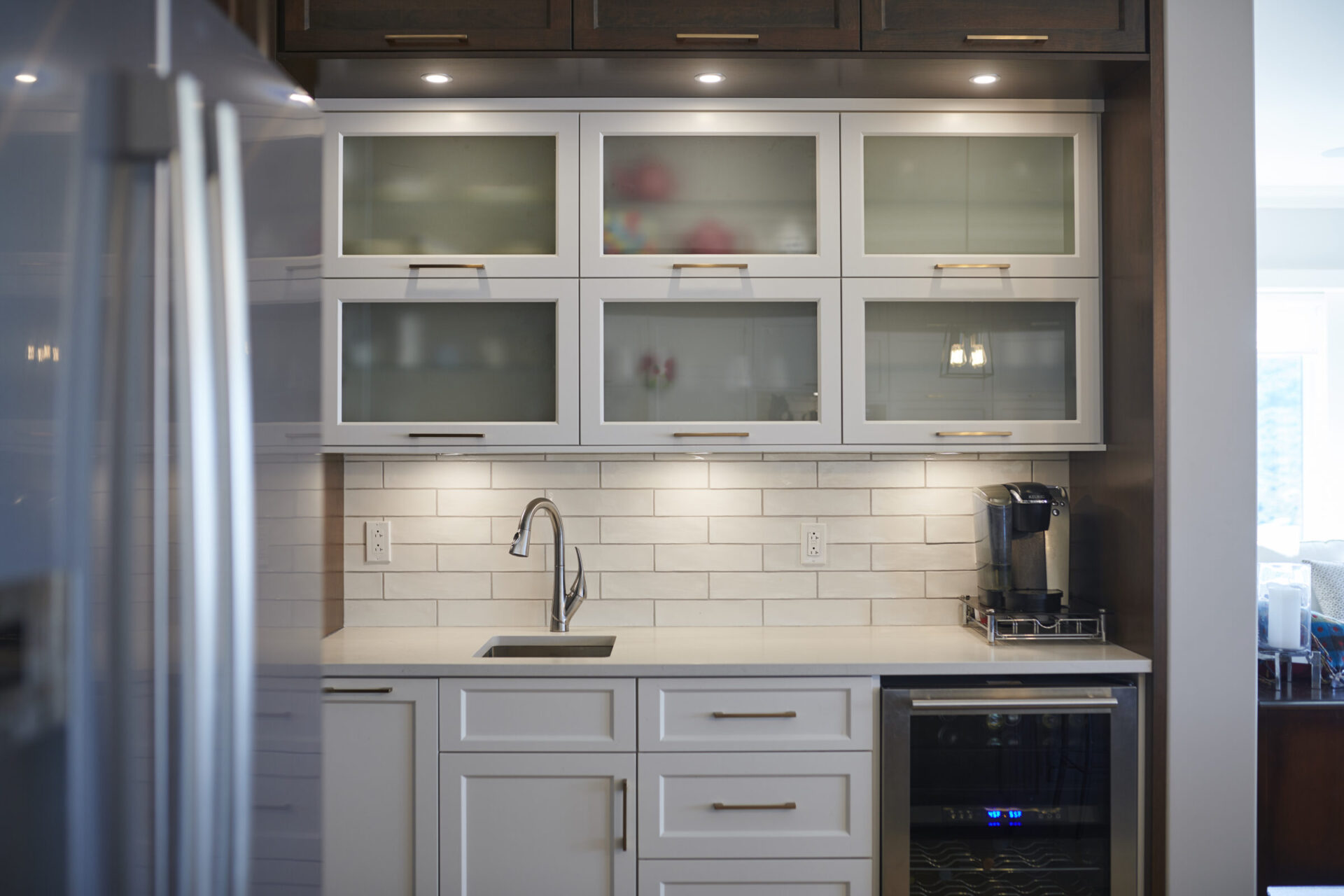 A modern kitchen with white cabinetry, frosted glass doors, a subway tile backsplash, stainless steel appliances, and a beverage cooler.