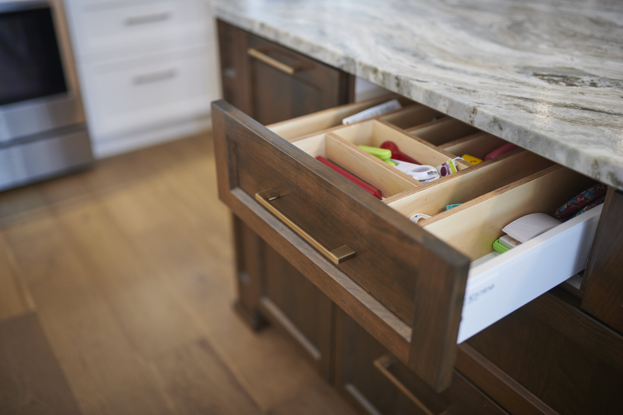 A kitchen drawer is partially open, revealing various utensils and organizers inside. The surrounding cabinets and countertops suggest a modern interior.