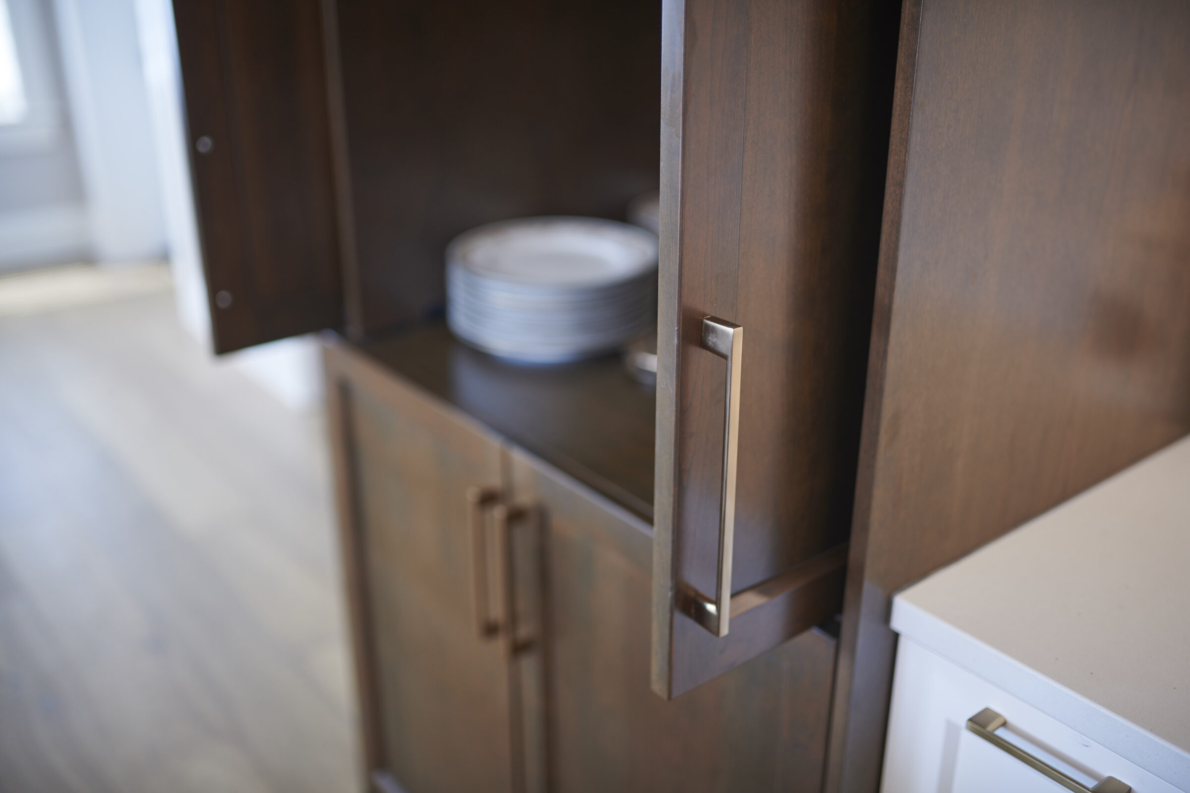 This image showcases an open wooden cabinet with a stack of white plates inside. It has modern handles, and part of a white countertop is visible.