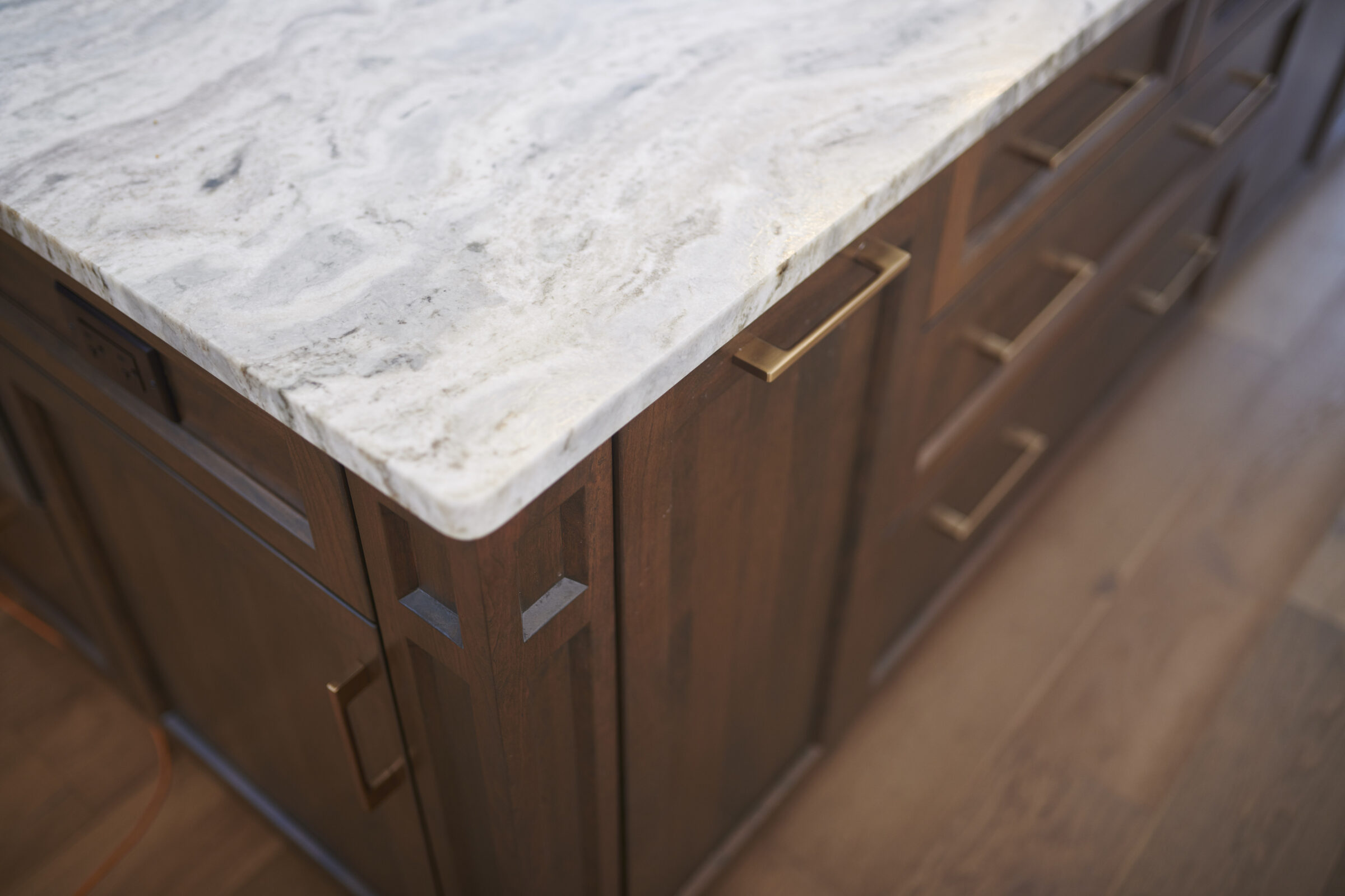 The image shows a close-up of a kitchen counter with a marble top and wooden cabinets featuring metallic handles, set against a hardwood floor background.