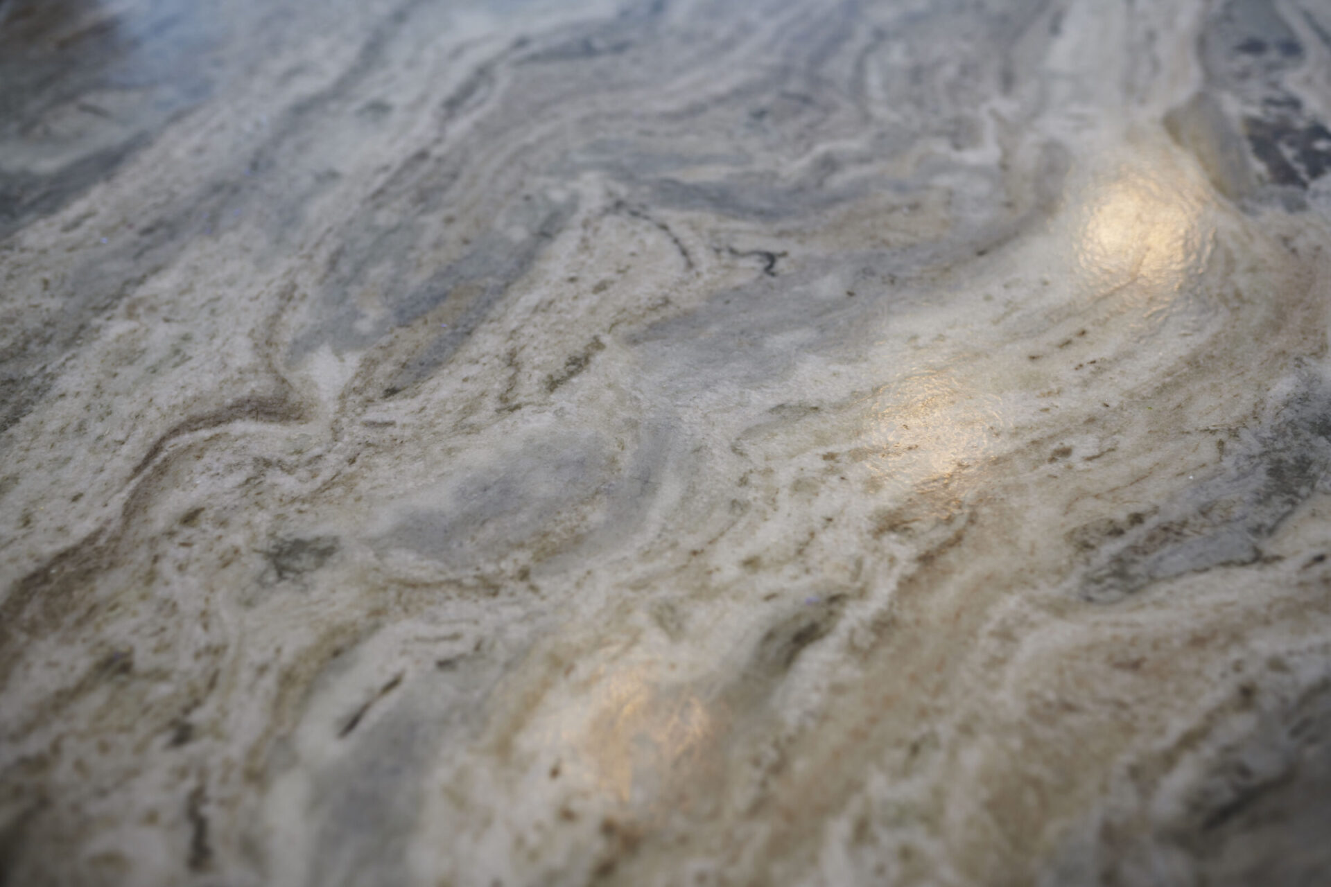 The image shows a close-up of a marble surface with intricate grey and white patterns, highlighted by soft, warm light reflections.