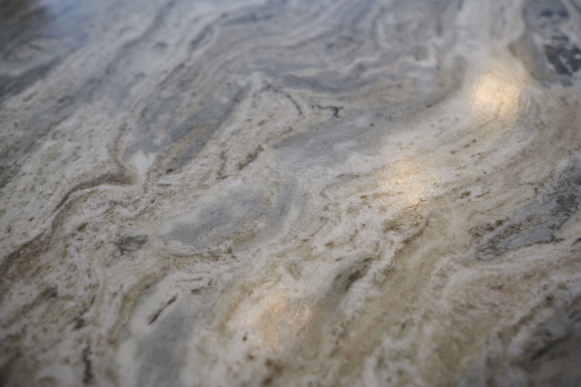 Close-up of a marble surface with intricate grey and white patterns, highlighted by soft, warm-toned light reflecting off the polished stone texture.