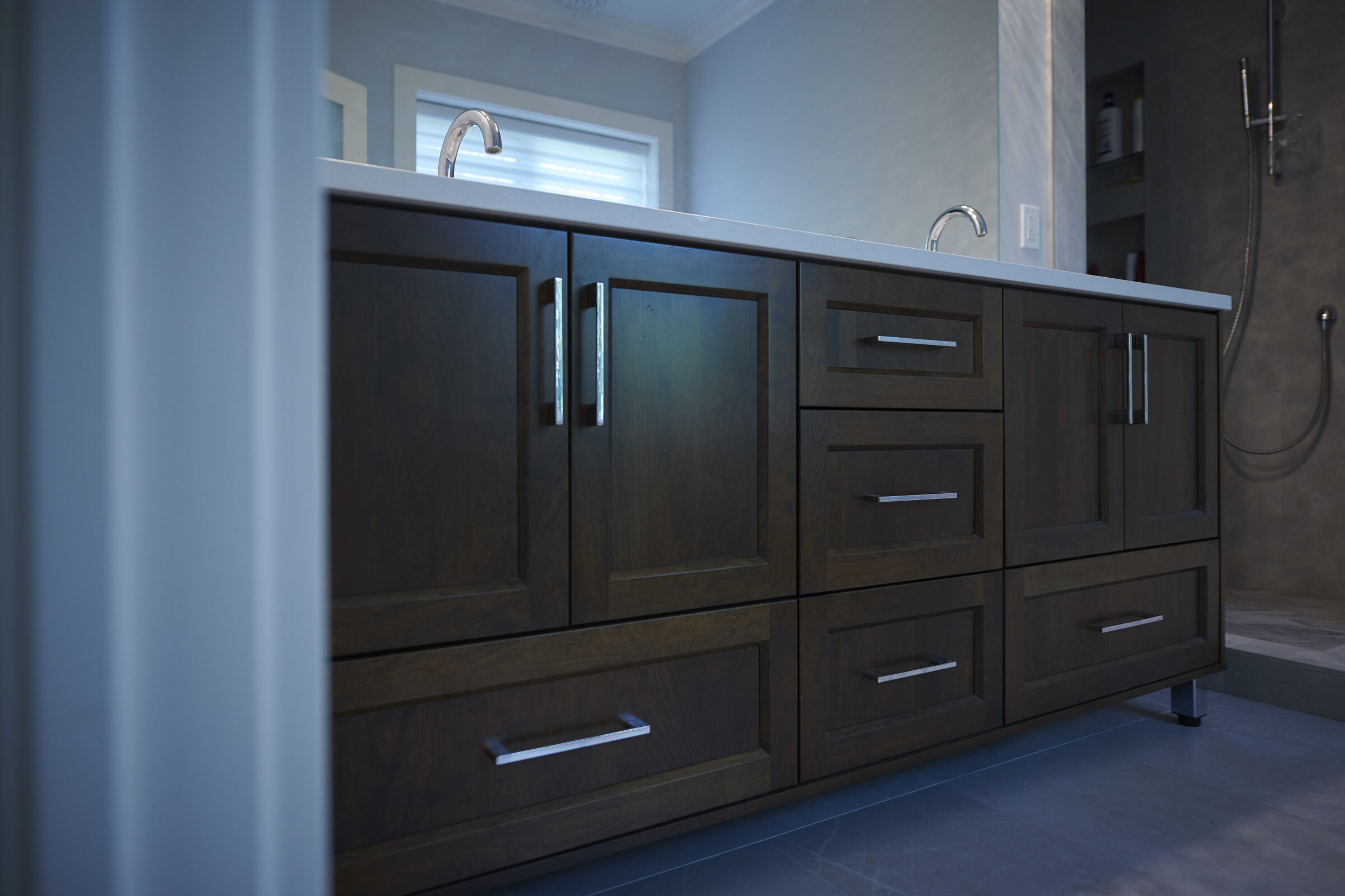 The image shows a modern bathroom vanity with dark wood cabinets and sleek metal handles, a countertop with an under-mount sink, and a mirror above.