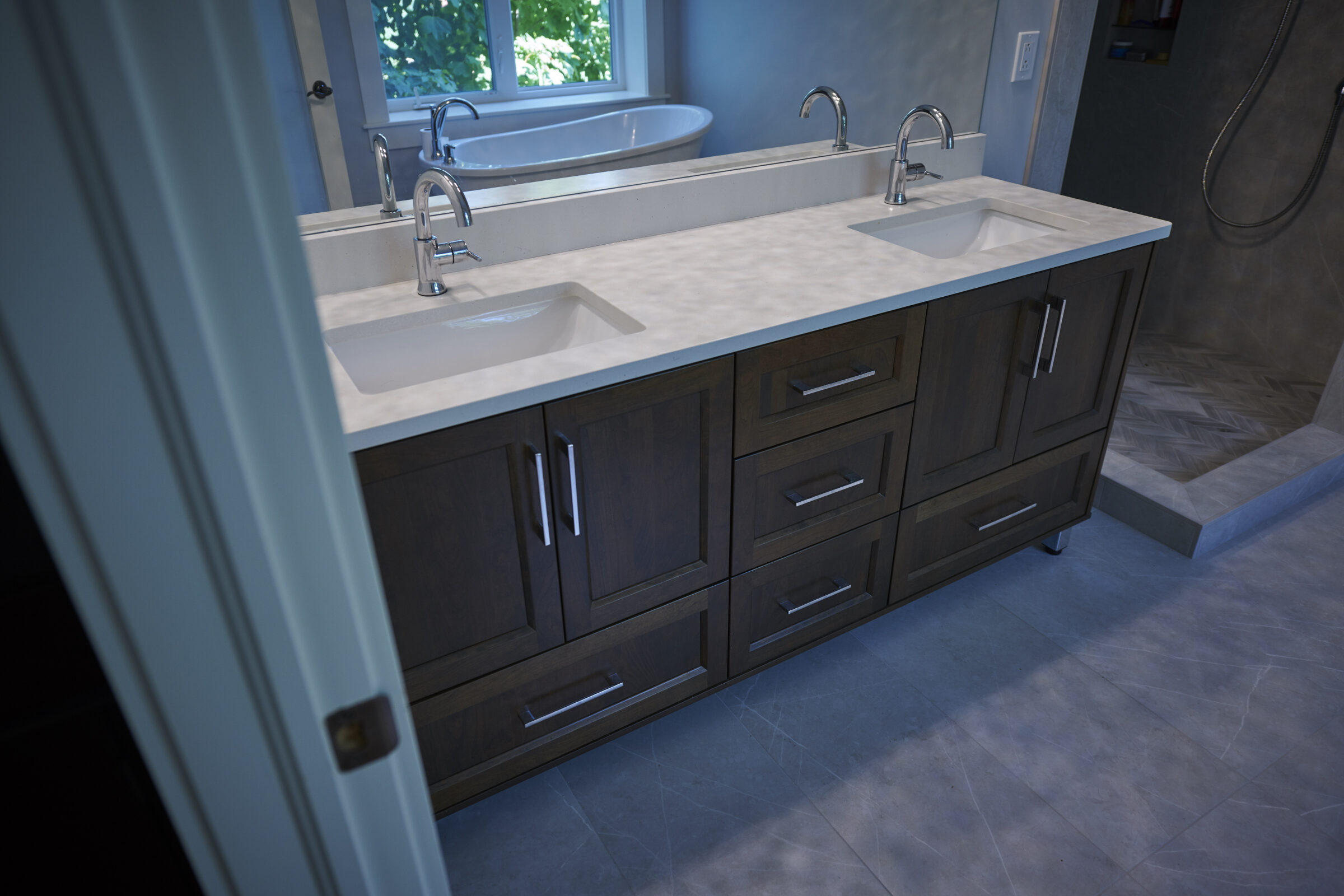 A modern bathroom featuring a dual-sink vanity with wooden cabinets and chrome faucets, under a large mirror, with a bathtub and sleek flooring visible.