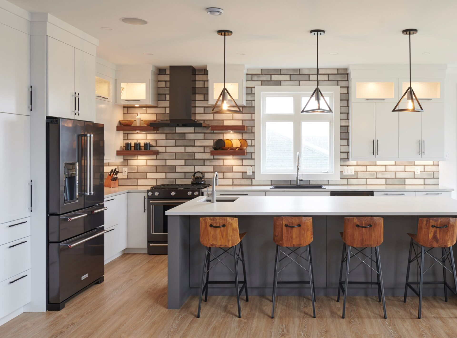 Modern kitchen with white cabinetry, wood accents, black appliances, and a large island with wooden barstools under geometric pendant lighting.
