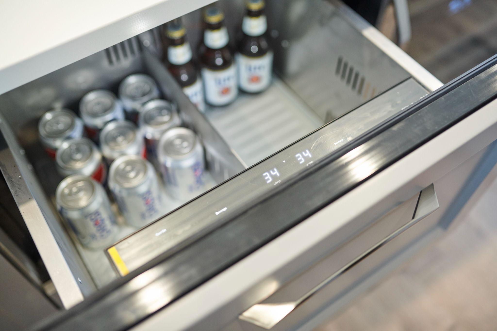 Beverage drawer fridge fully open, showing soda cans and beer bottles neatly organized with digital temperature control set to 34°F.