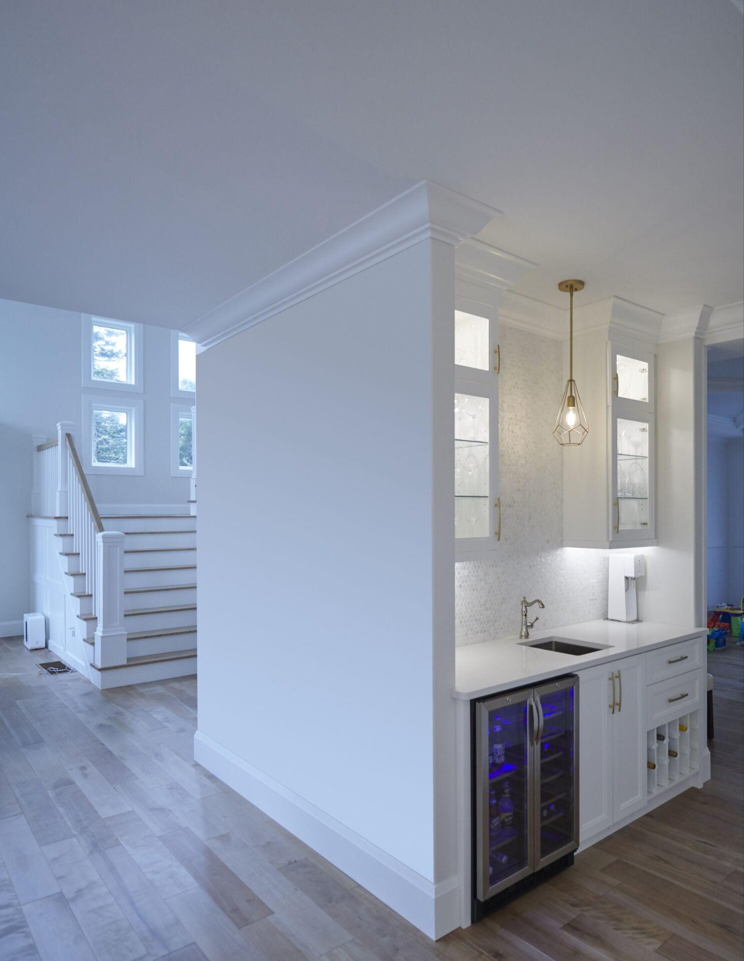 Built-in home bar with white cabinetry, quartz countertop, wine storage, under-counter beverage cooler with blue lighting, and hanging pendant light.