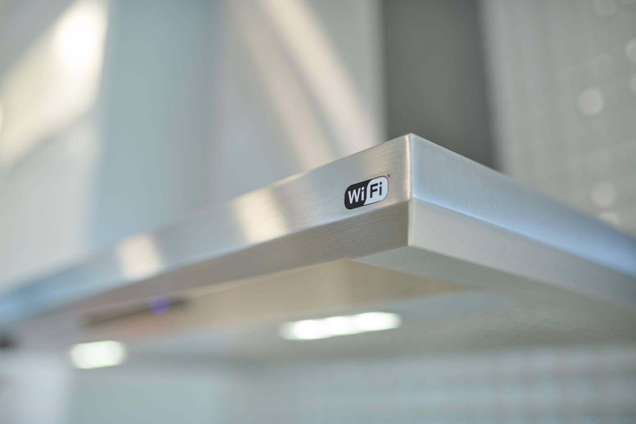 Close-up of a stainless steel range hood in a modern kitchen with a Wi-Fi connectivity label on the edge.