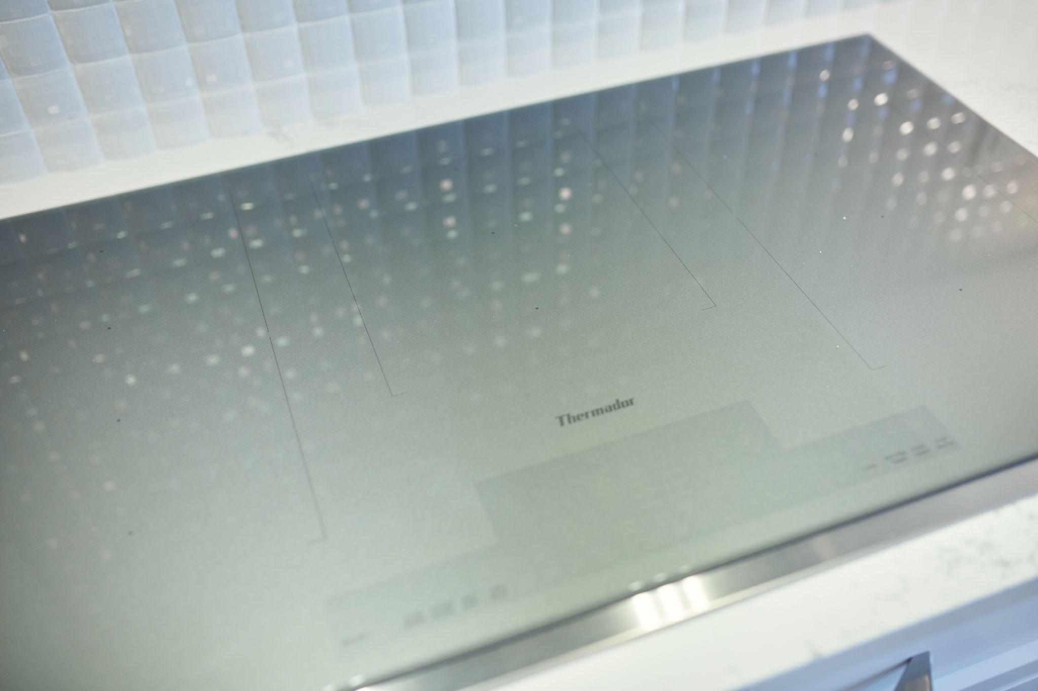 Sleek Thermador induction cooktop with a smooth glass surface reflecting backsplash lighting.
