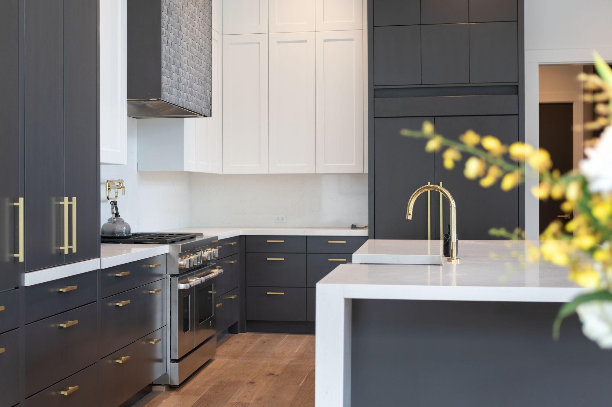 Dark charcoal shaker and slab kitchen with white uppers, gold hardware, and professional range