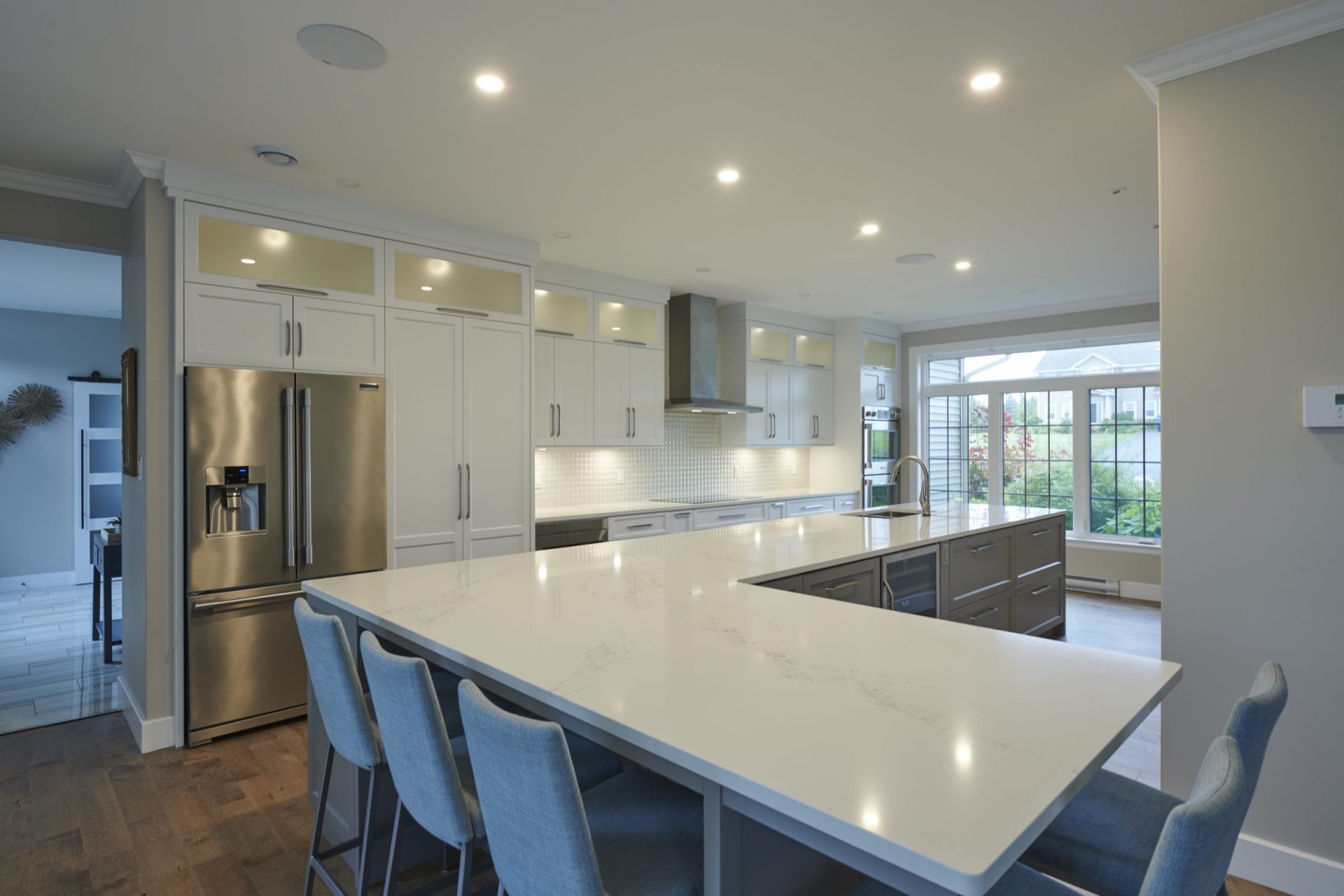 Modern open-concept kitchen featuring a large wrap-around island, blue barstools, and built-in stainless steel appliances.