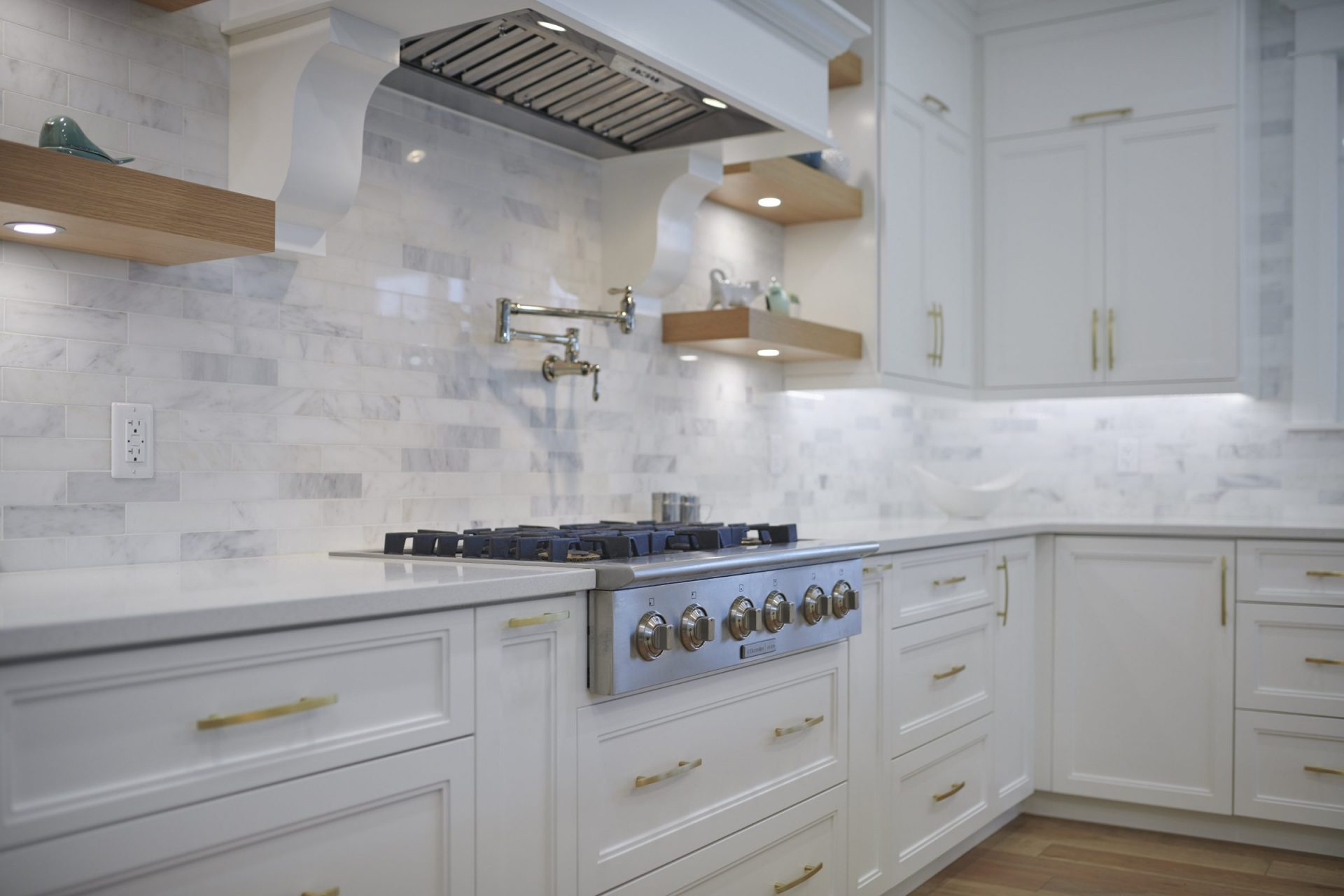 Traditional kitchen design featuring white recessed-panel cabinetry, a marble backsplash, and floating wood shelves.
