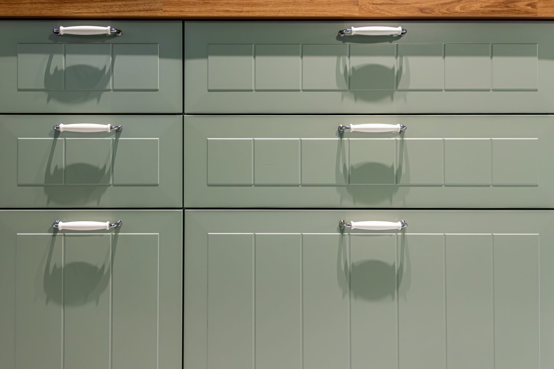 Custom sage green beadboard cabinets with white ceramic and chrome handles.