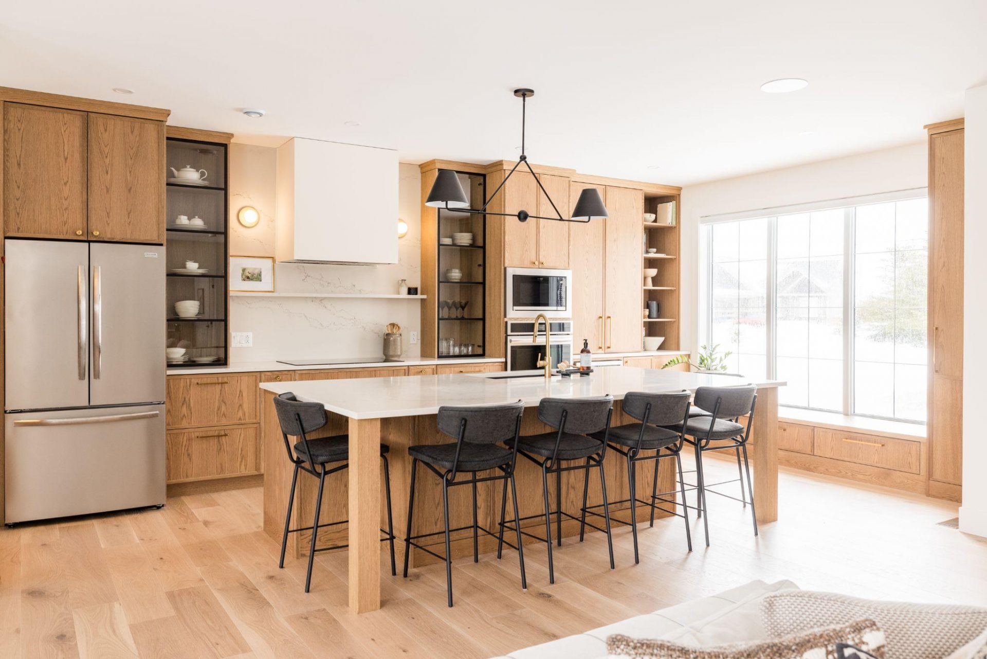 Natural oak slab kitchen with white island, open shelving, black pendants, and light wood floors