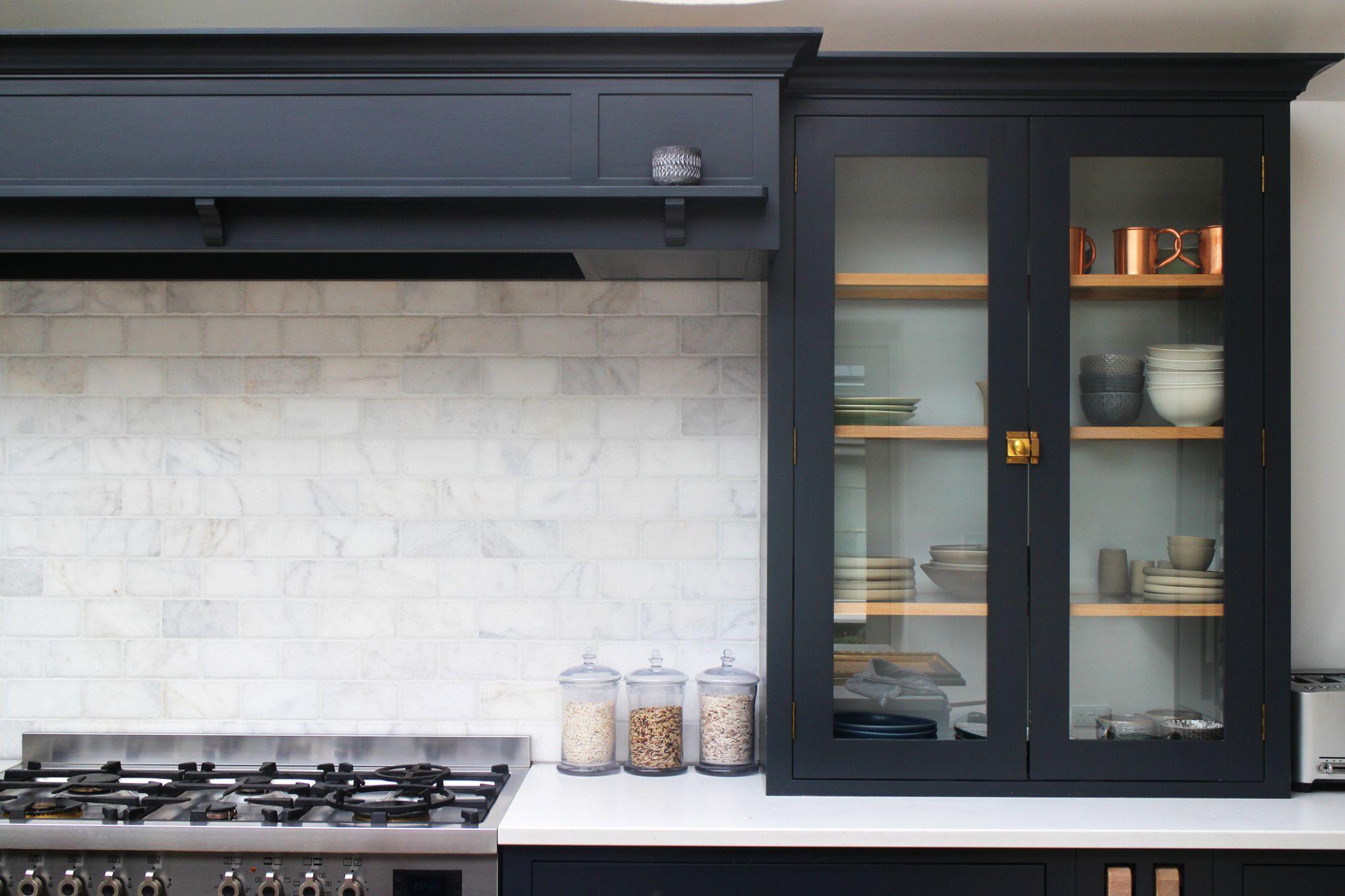 Navy shaker upper cabinet with glass doors open displaying dishes and copper mugs